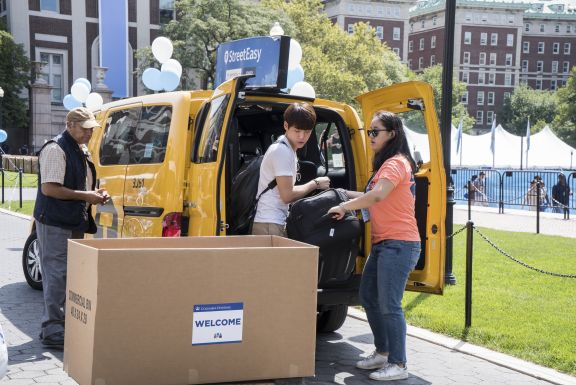 Orientation leader helping a student move items out of a taxi